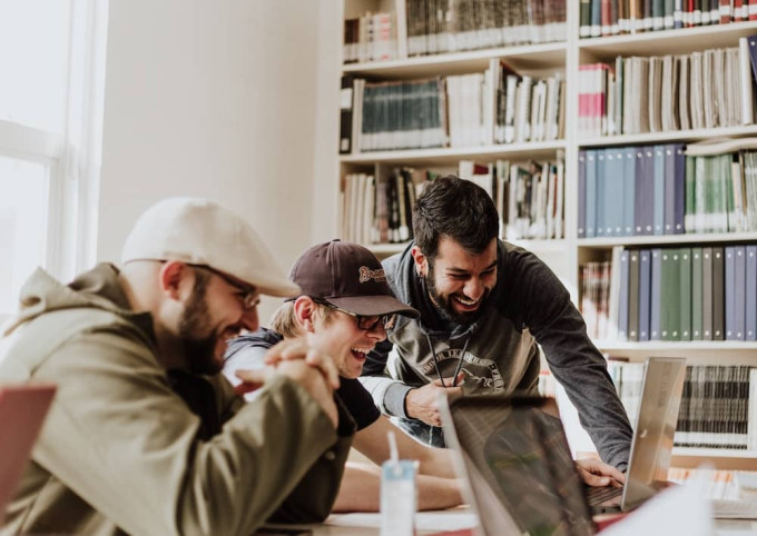 Three men gathered around a laptop, laughing and enjoying what they're hearing