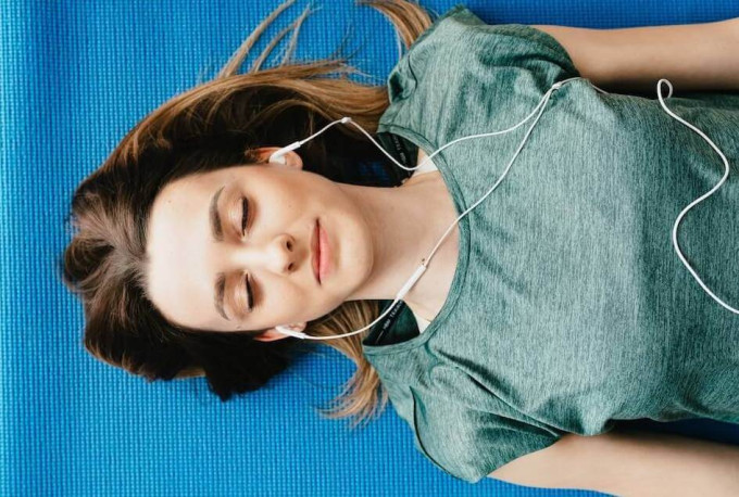 Young woman relaxing on yoga mat with eyes closed and earbuds in her ears