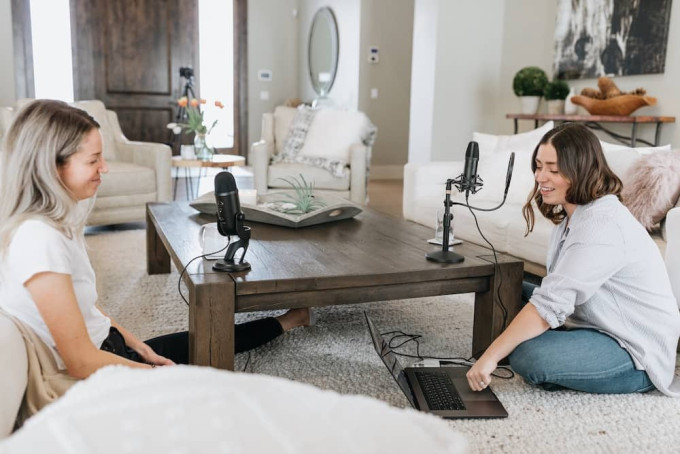 Two women recording a podcast on a lounge room floor