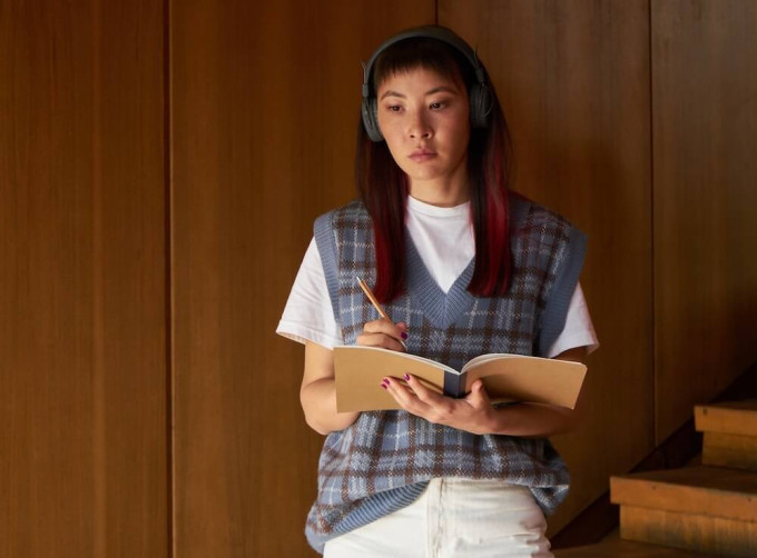 Young woman wearing headphones and holding notebook, figuring out how to structure a podcast