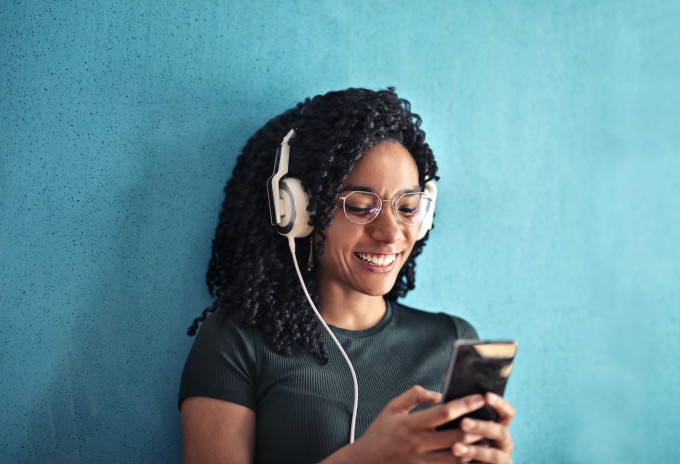 woman with phone in hand and headphones, smiling to show browsing podcast rankings