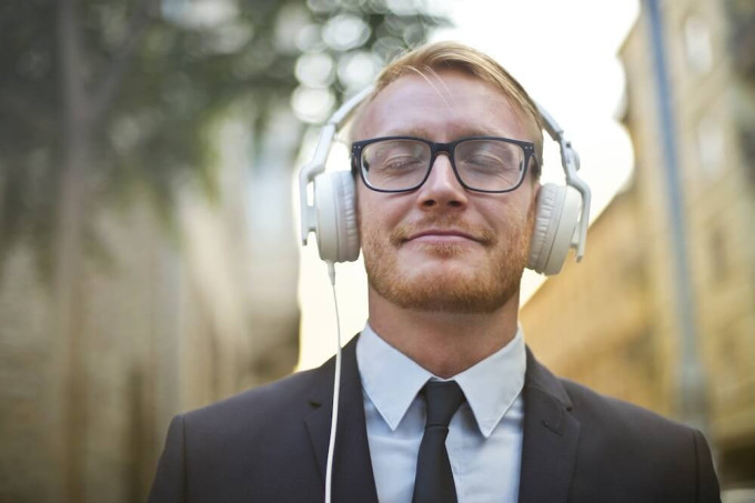 Young guy in suit wearing white headphones, eyes closed and enjoying what he's listening to