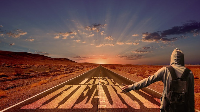 Hitchhiker on open road leading to sunrise