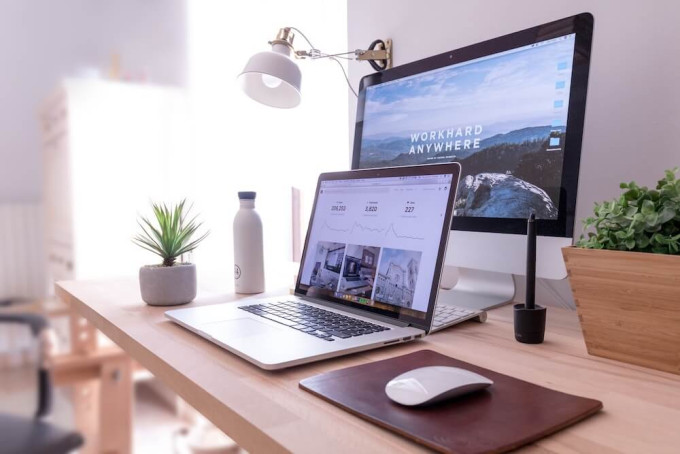 Laptop on desk with big screen behind it