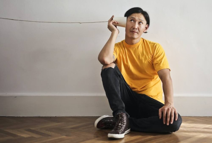 Man sitting on the ground pretending to listen through a cup and string