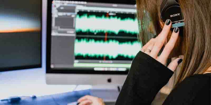 Young woman with headphones on editing a podcast