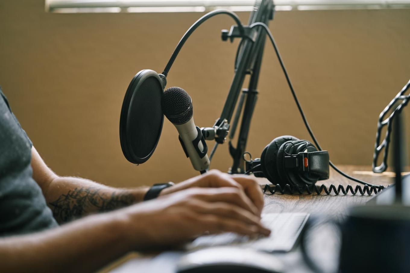 podcast microphone attached to a boom arm on a desk in from of someone editing on a computer, podcast agency producer